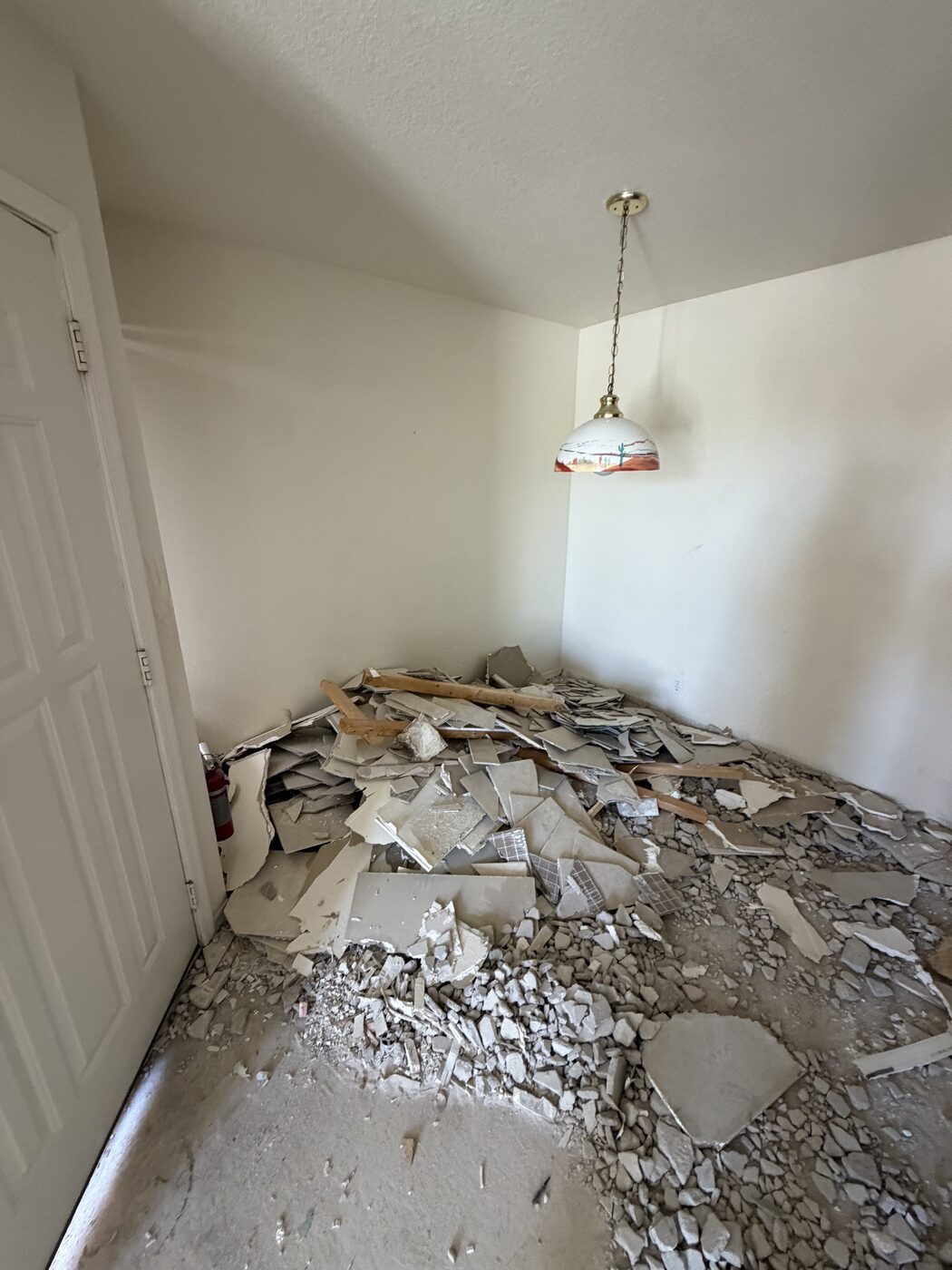 Interior room with a large pile of broken tile and drywall stacked against the wall during demolition