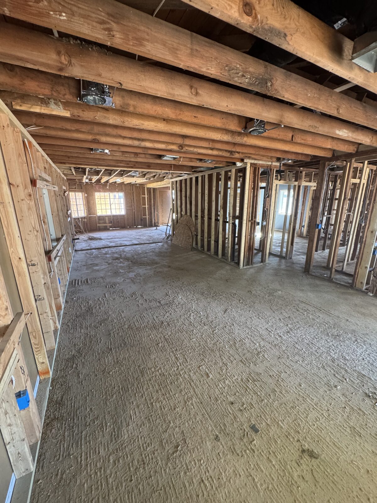 Whole-house interior demolition down to open wood framing and exposed ceiling joists with a clean concrete slab