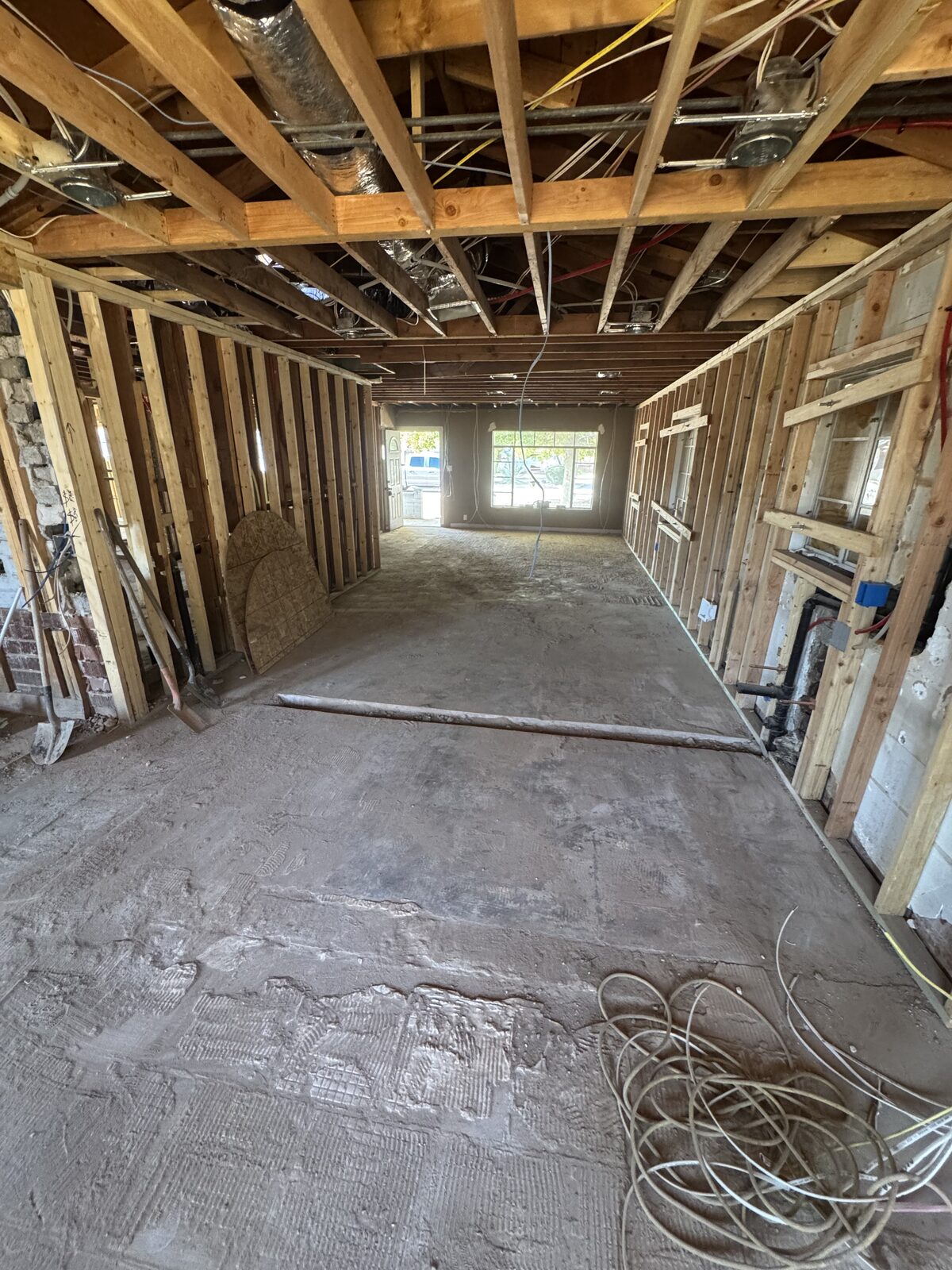 Gutted living area taken to the studs with ductwork and wiring exposed overhead and the slab swept clean